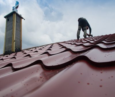 Roofer working on roof structure of building on construction site,Roofer using air or pneumatic nail gun and installing Metal Sheet on top new roof.